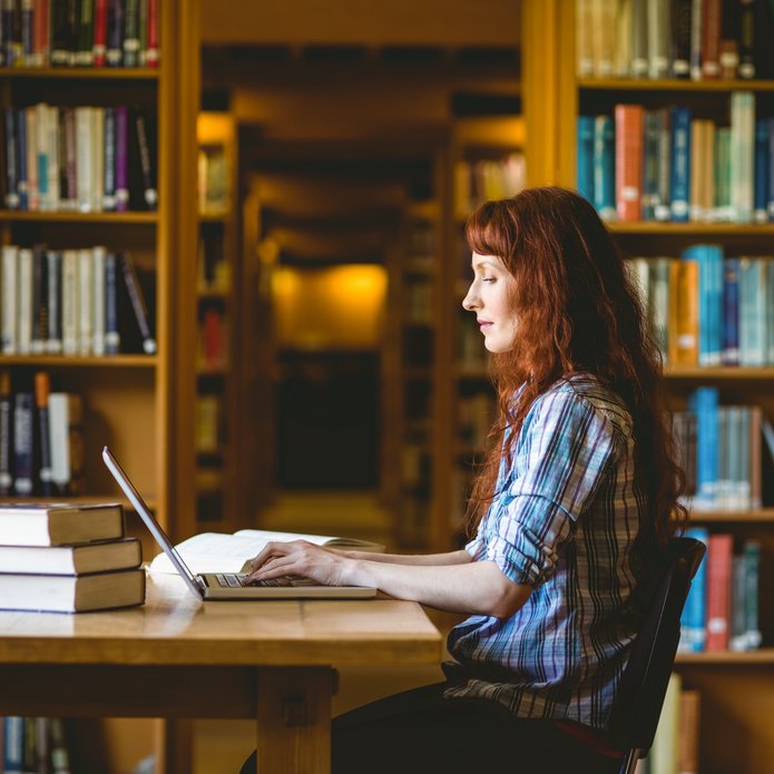 kolorowe zdjęcie przedstawia młodą studentkę pracującą w bibliotece