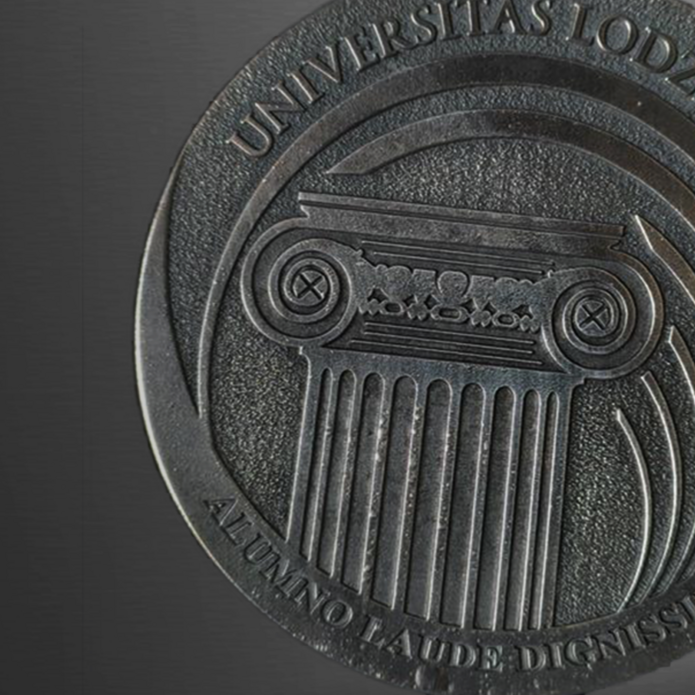 Okrągły medal metalowy z wytłoczonymi detalami: na górnej połowie napis „UNIVERSITAS LODZIENSIS” wzdłuż krawędzi. W centralnej części stylizowana kolumna dorycka z bogato zdobionym kapitelem. Na dolnej części medaliony wpisano sentencję „ALUMNO LAUDE DIGNISSIMO”. Tło reliefowe o drobnej fakturze podkreśla wyryte elementy – napisy i kolumnę.