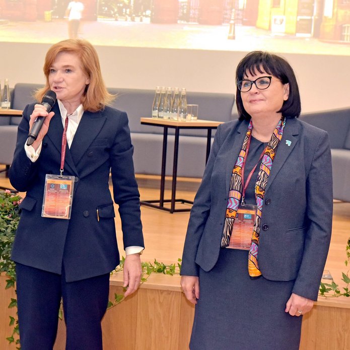 trzy kobiety stoją w auli i przemawiają 