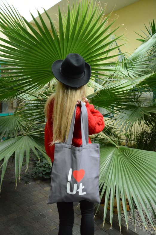Odwrócona tyłem dziewczyna z płócienną torbą UŁ stoi na tle palmy 